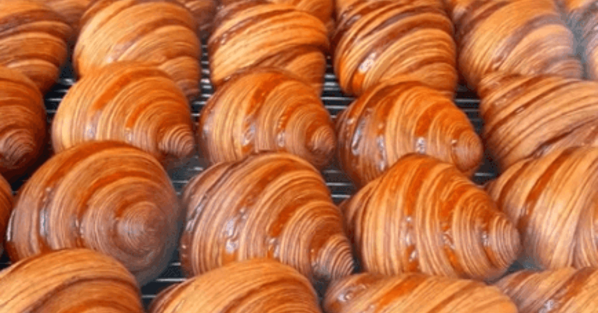 A tray of freshly baked golden-brown croissants with a shiny glaze, displaying their flaky, layered texture.