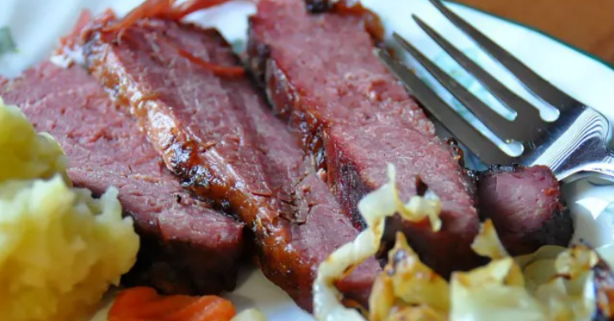 Slices of juicy canned corned beef served with sautéed cabbage and mashed vegetables on a white plate with a fork