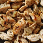 Hands shredding leftover rotisserie chicken with forks on a wooden cutting board.