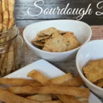 A variety of dishes made from sourdough discard, including pancakes, cookies, and crackers, arranged on a rustic wooden table.