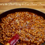 A bowl of baked beans garnished with fresh parsley, served with toasted bread on a rustic wooden table.