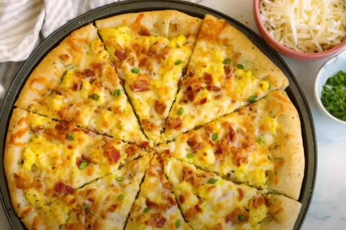 A freshly baked breakfast pizza topped with scrambled eggs, bacon, cheese, and fresh herbs on a wooden serving board.