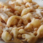 Golden-brown funnel cake with powdered sugar on a plate, highlighting perfect swirls and crispy texture.