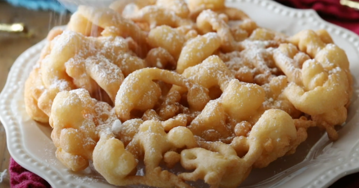 Golden-brown funnel cake with powdered sugar on a plate, highlighting perfect swirls and crispy texture.